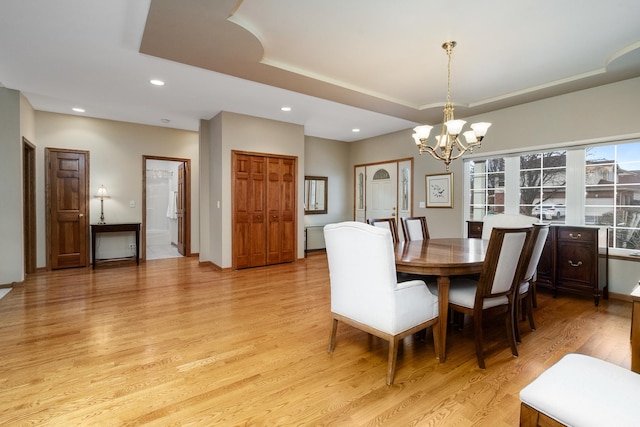 dining area with an inviting chandelier, a tray ceiling, and light hardwood / wood-style flooring