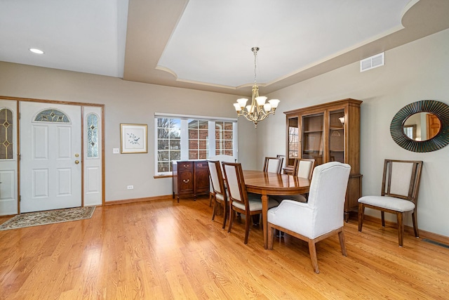 dining space featuring a notable chandelier, light wood-type flooring, and a tray ceiling