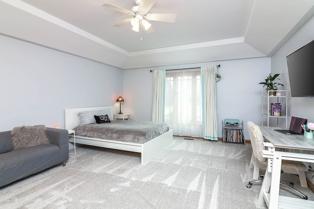 carpeted bedroom with a raised ceiling and ceiling fan