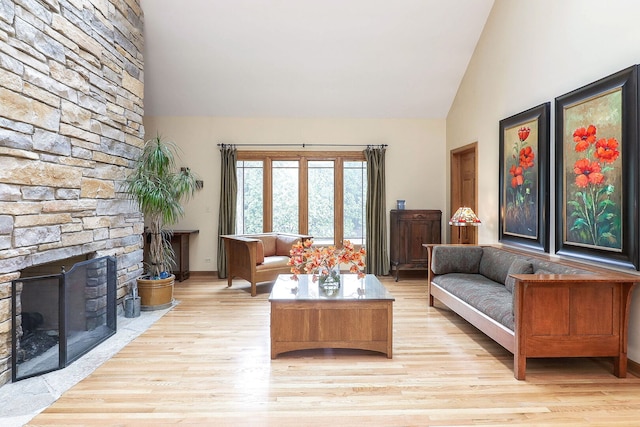living room featuring a stone fireplace, light wood-style floors, and high vaulted ceiling