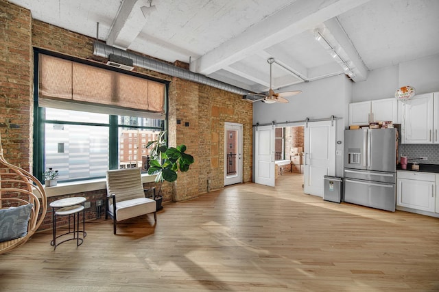 interior space featuring a barn door, stainless steel fridge with ice dispenser, brick wall, backsplash, and a towering ceiling