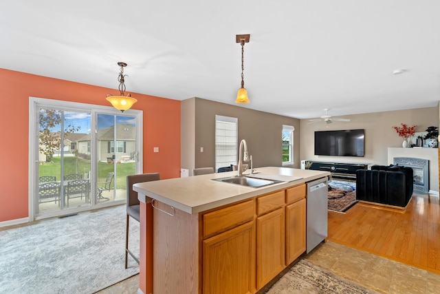 kitchen featuring light wood-type flooring, a kitchen island with sink, sink, decorative light fixtures, and dishwasher