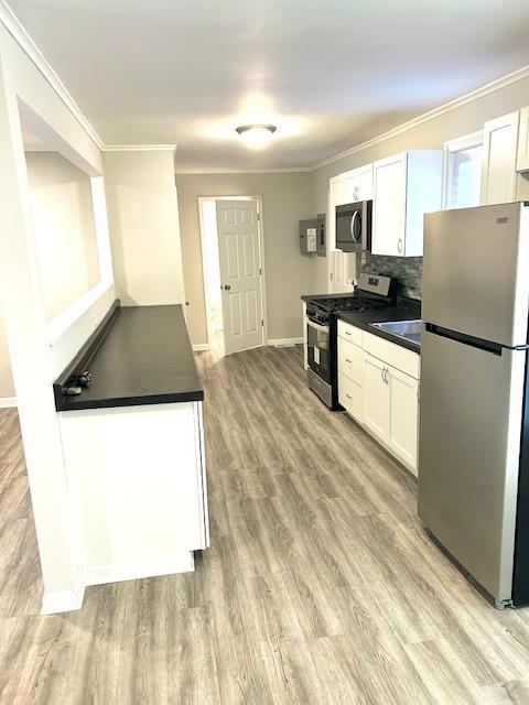 kitchen featuring decorative backsplash, appliances with stainless steel finishes, crown molding, light hardwood / wood-style flooring, and white cabinets