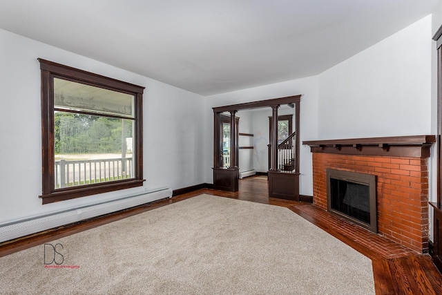 unfurnished living room with dark wood-type flooring, baseboard heating, and a brick fireplace