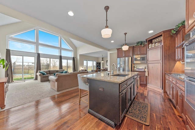 kitchen featuring appliances with stainless steel finishes, light stone counters, sink, pendant lighting, and a center island with sink