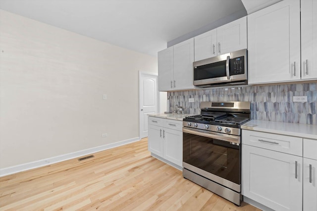 kitchen with backsplash, light hardwood / wood-style flooring, appliances with stainless steel finishes, light stone counters, and white cabinetry