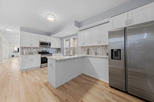 kitchen featuring kitchen peninsula, appliances with stainless steel finishes, decorative backsplash, light hardwood / wood-style floors, and white cabinetry