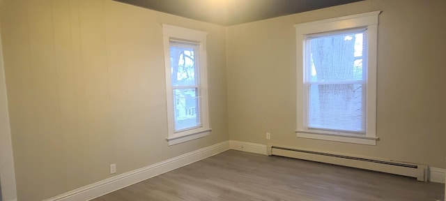 empty room with baseboard heating, a wealth of natural light, and wood-type flooring