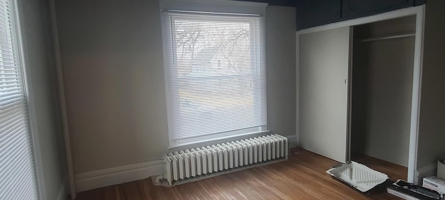 unfurnished bedroom with wood-type flooring, radiator heating unit, and a closet