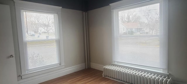 empty room with hardwood / wood-style floors, radiator heating unit, and a healthy amount of sunlight