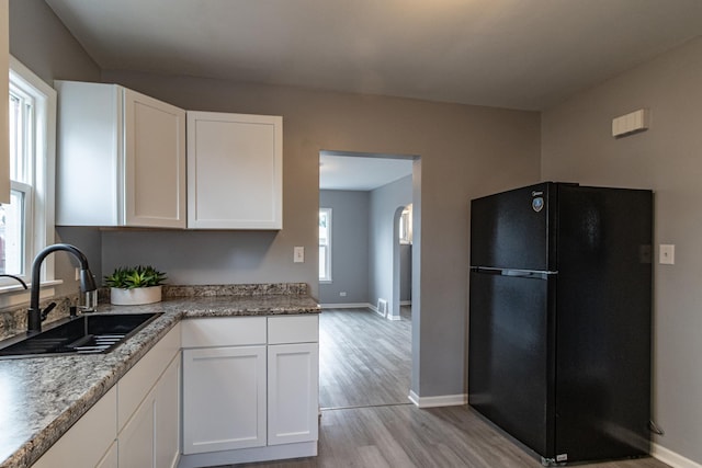 kitchen with black refrigerator, white cabinetry, a healthy amount of sunlight, and sink