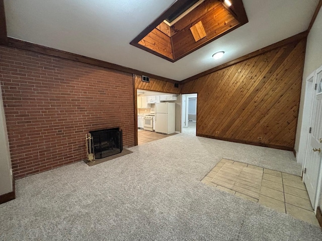 unfurnished living room featuring vaulted ceiling with skylight, light carpet, wooden walls, and a brick fireplace