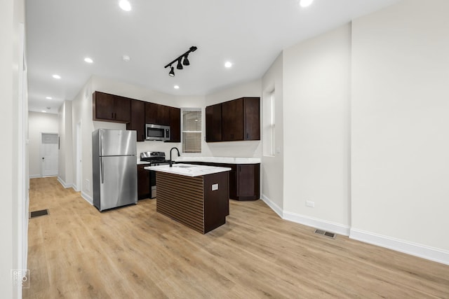 kitchen with dark brown cabinetry, light hardwood / wood-style flooring, an island with sink, a breakfast bar area, and appliances with stainless steel finishes