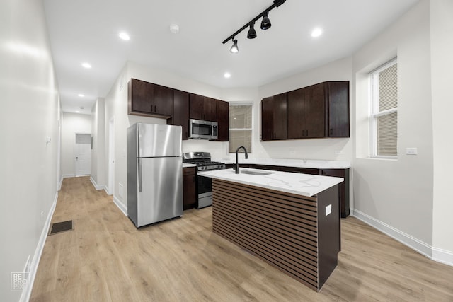 kitchen with a kitchen island with sink, sink, light hardwood / wood-style floors, dark brown cabinetry, and stainless steel appliances