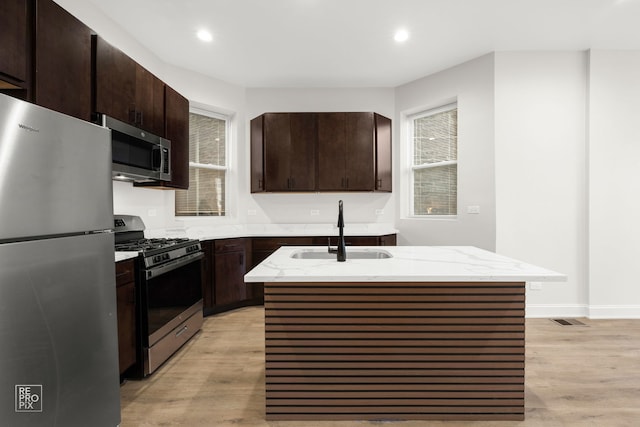 kitchen with sink, light wood-type flooring, a kitchen island with sink, and appliances with stainless steel finishes