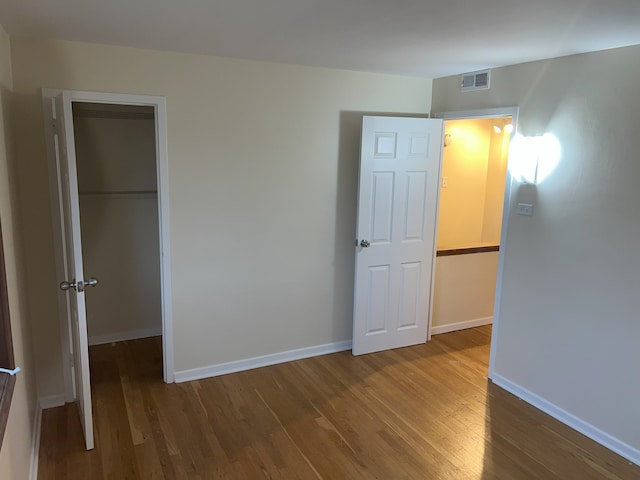 unfurnished bedroom with wood-type flooring, a spacious closet, and a closet