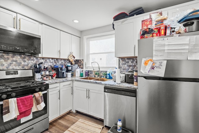 kitchen with backsplash, white cabinets, sink, light stone countertops, and stainless steel appliances