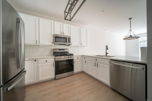 kitchen with pendant lighting, white cabinets, sink, light wood-type flooring, and stainless steel appliances