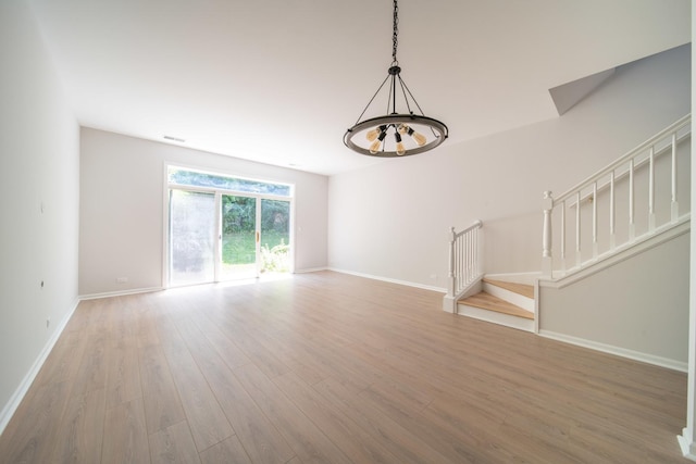 unfurnished living room with wood-type flooring and an inviting chandelier