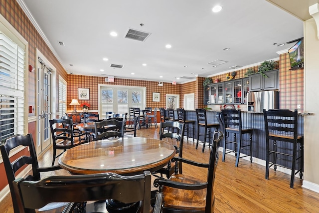 dining area with bar area, crown molding, french doors, and light wood-type flooring