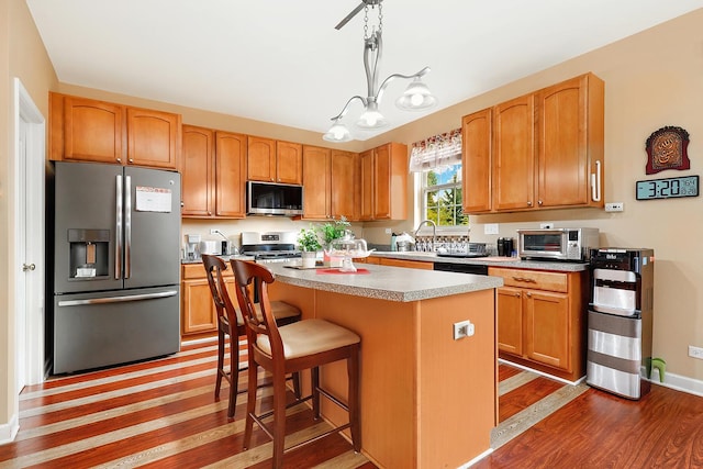 kitchen with pendant lighting, hardwood / wood-style flooring, stainless steel appliances, a center island, and a kitchen breakfast bar