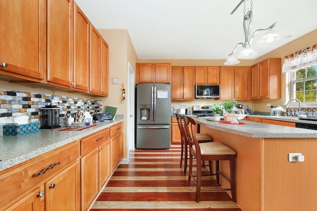 kitchen featuring light hardwood / wood-style flooring, appliances with stainless steel finishes, a kitchen island, pendant lighting, and decorative backsplash