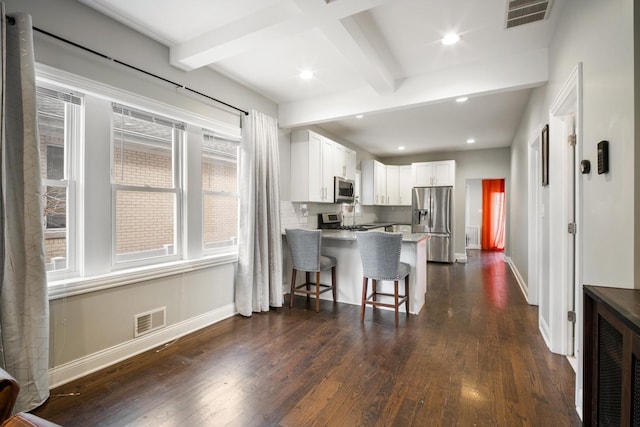 kitchen featuring kitchen peninsula, appliances with stainless steel finishes, dark wood-type flooring, white cabinetry, and a breakfast bar area