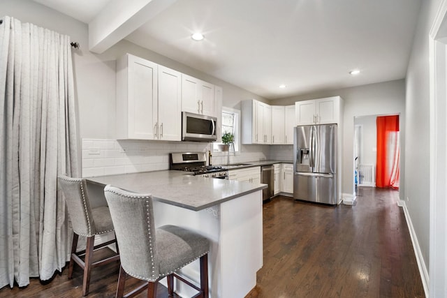 kitchen with kitchen peninsula, a breakfast bar, stainless steel appliances, dark wood-type flooring, and white cabinetry