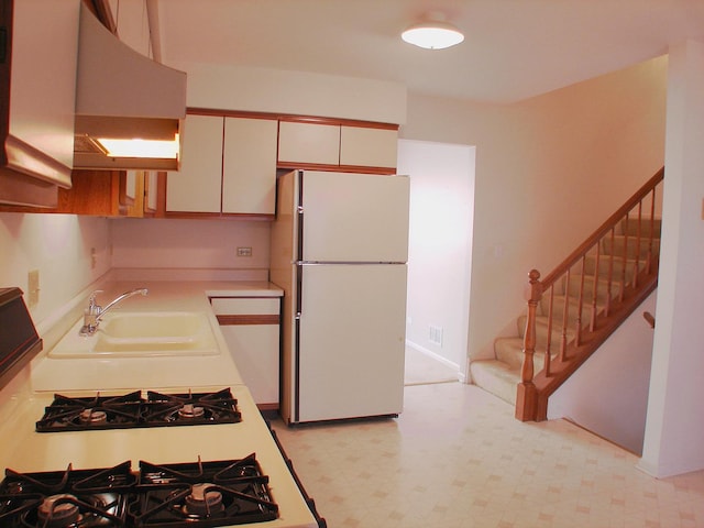 kitchen with white refrigerator, sink, range hood, gas stove, and white cabinetry