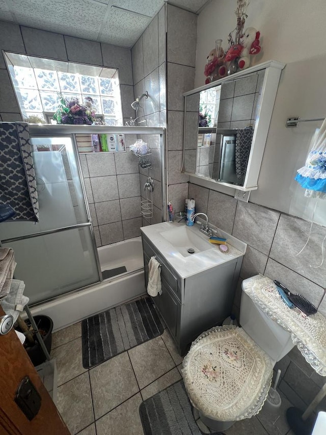 bathroom featuring a drop ceiling, tile patterned flooring, vanity, a shower with shower door, and tile walls