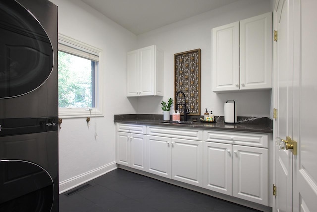 kitchen with stacked washer and dryer, white cabinets, and sink