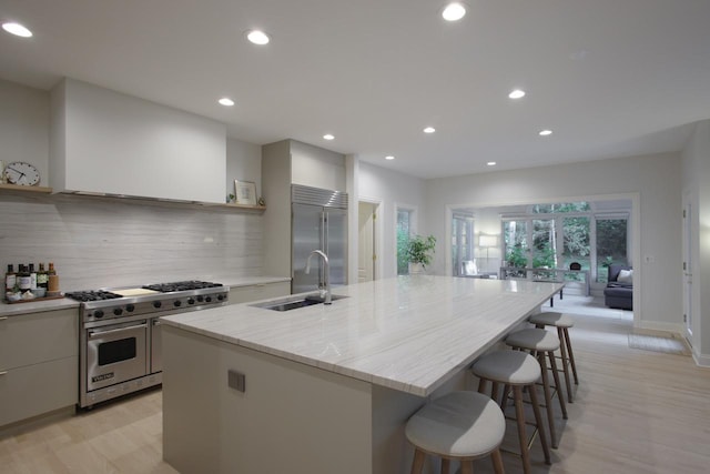 kitchen with an island with sink, tasteful backsplash, high quality appliances, light stone counters, and sink