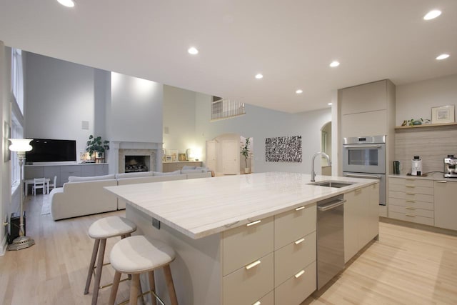 kitchen with a kitchen bar, appliances with stainless steel finishes, a kitchen island with sink, light wood-type flooring, and sink