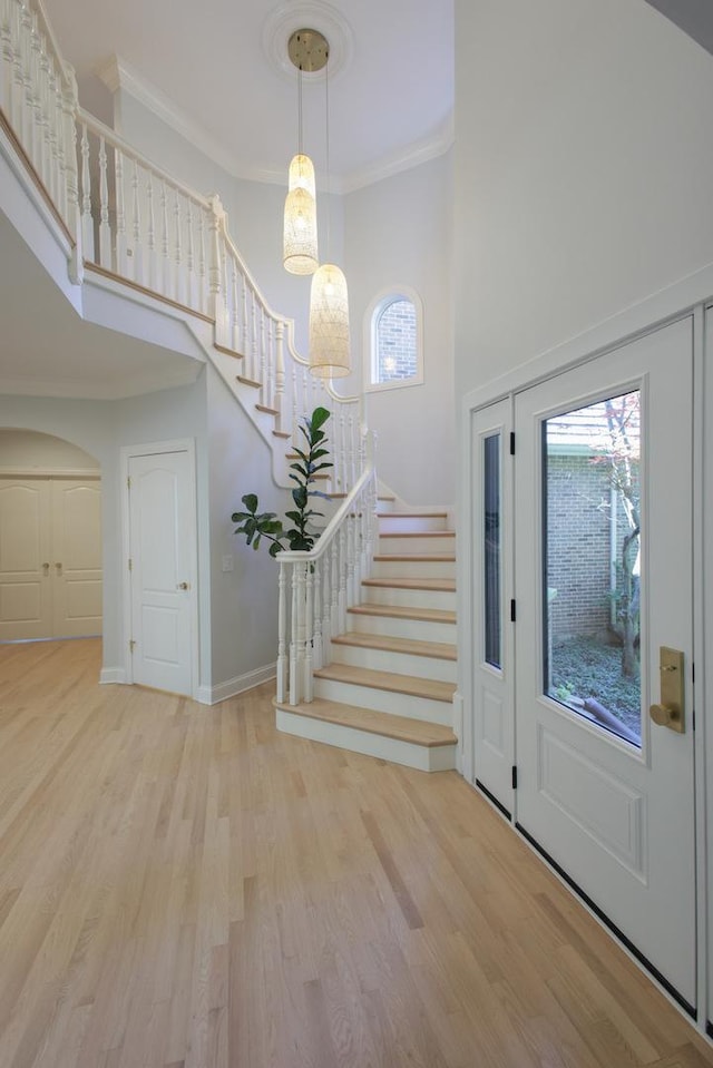 foyer featuring a high ceiling, ornamental molding, and light wood-type flooring