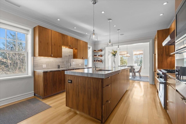 kitchen featuring pendant lighting, sink, a kitchen island with sink, ornamental molding, and wall chimney exhaust hood