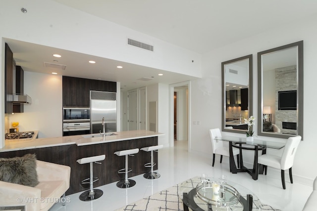 kitchen with wall chimney exhaust hood, kitchen peninsula, built in appliances, a fireplace, and a breakfast bar