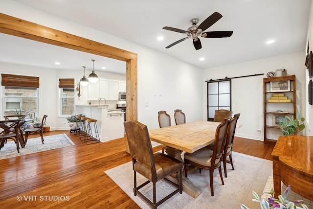 dining area featuring a barn door, light hardwood / wood-style floors, ceiling fan, and sink