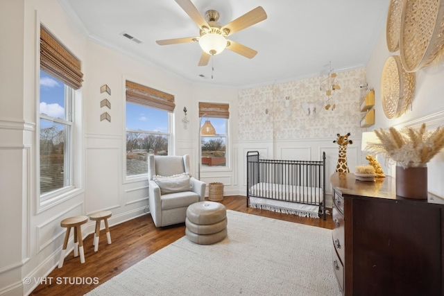 bedroom with crown molding, ceiling fan, a nursery area, and dark hardwood / wood-style floors