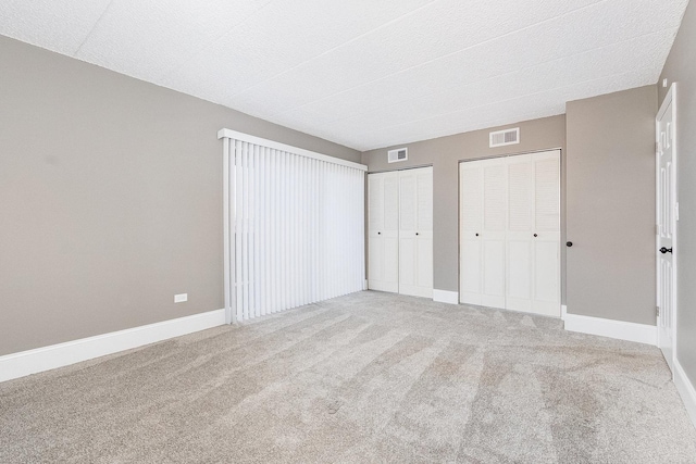 unfurnished bedroom with baseboards, visible vents, carpet flooring, and two closets