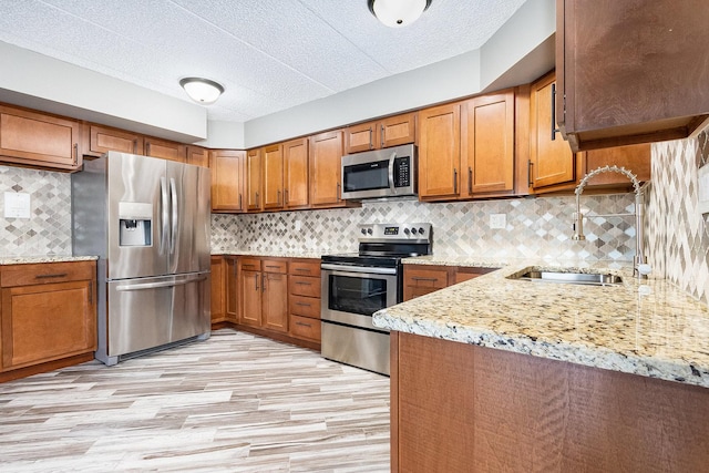 kitchen featuring tasteful backsplash, appliances with stainless steel finishes, brown cabinetry, a sink, and light stone countertops