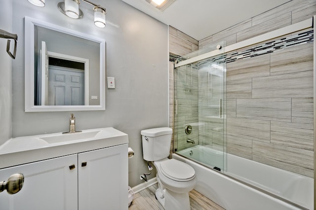 full bathroom with combined bath / shower with glass door, vanity, hardwood / wood-style flooring, and toilet