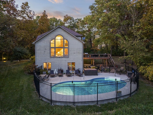 pool at dusk featuring a jacuzzi, a patio, and a lawn