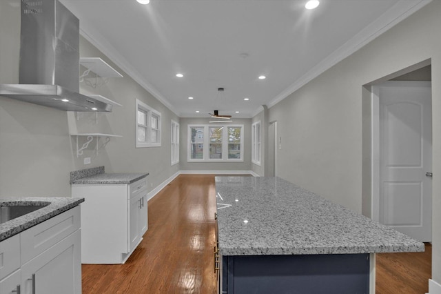 kitchen featuring wall chimney exhaust hood, an island with sink, hardwood / wood-style flooring, white cabinets, and ornamental molding