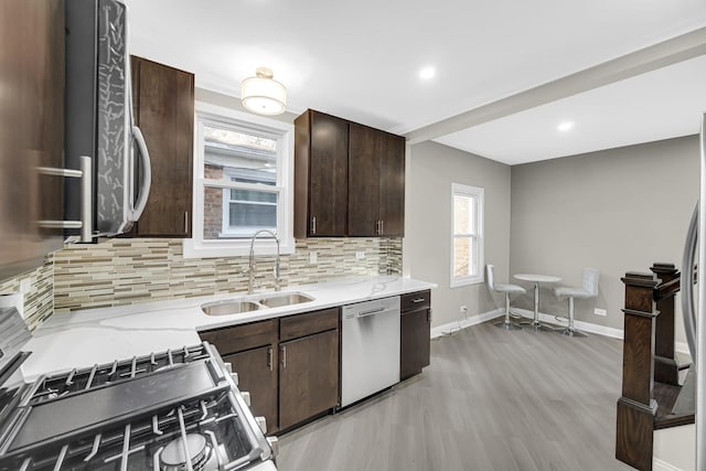 kitchen featuring light stone countertops, dark brown cabinets, sink, light hardwood / wood-style flooring, and dishwasher