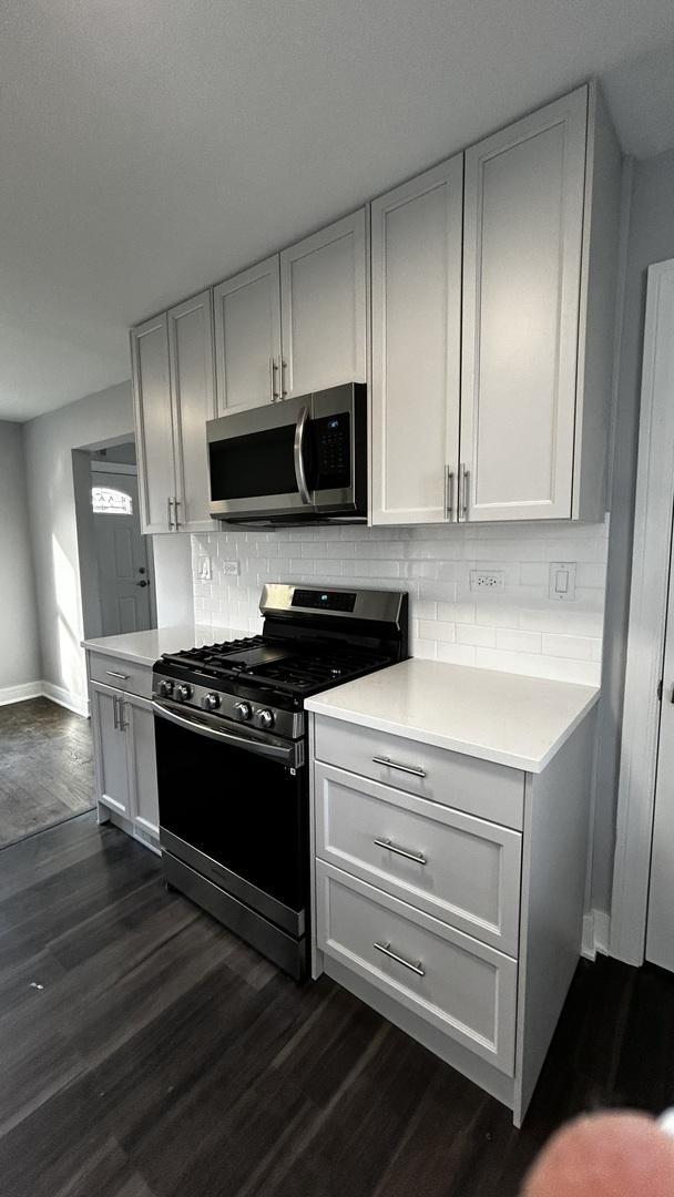 kitchen featuring white cabinets, backsplash, stainless steel appliances, and dark wood-type flooring