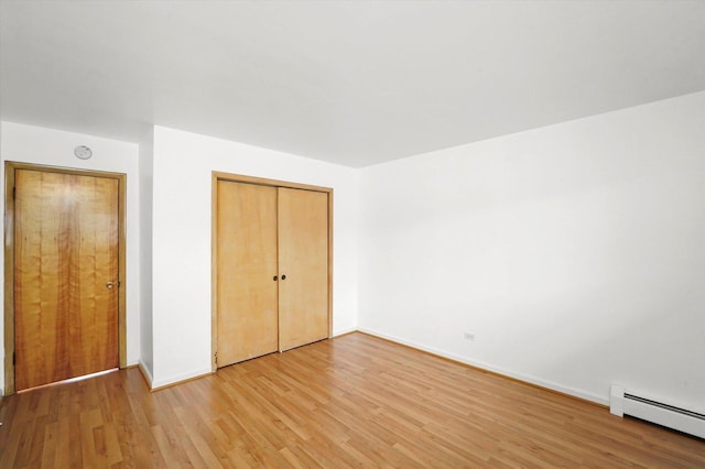 unfurnished bedroom with a closet, wood-type flooring, and a baseboard radiator