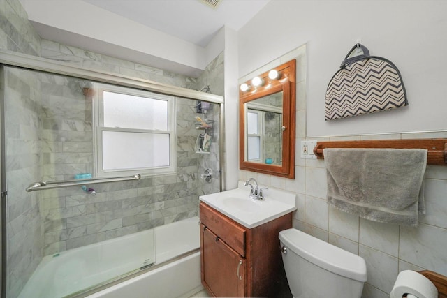 full bathroom featuring vanity, toilet, shower / bath combination with glass door, and tile walls