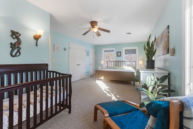 bedroom featuring a crib, light colored carpet, a closet, and ceiling fan