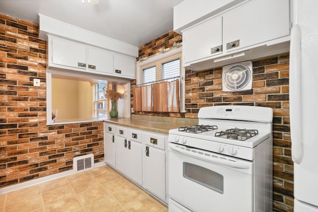 kitchen featuring white cabinetry, white gas stove, and brick wall