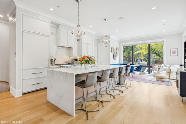 kitchen with a kitchen island with sink, light hardwood / wood-style flooring, decorative light fixtures, white cabinetry, and a breakfast bar area